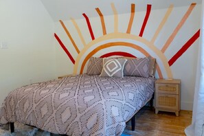 A bedroom with a patterned bedspread, a headboard with a sun-like design, and a nightstand with drawers. - 3BR Saint Jo Getaway | BBQ, Fire Pit + Comfort (Saint Jo)