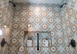 A bathroom with patterned tiles, a glass shower enclosure, and toiletries on a shelf. - 3BR Saint Jo Getaway | BBQ, Fire Pit + Comfort (Saint Jo)