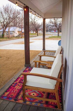 A covered porch with wooden chairs and a colorful rug. - 3BR Saint Jo Getaway | BBQ, Fire Pit + Comfort (Saint Jo)
