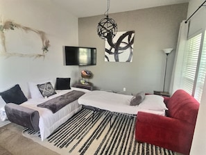 Un dormitorio moderno con una cama, una silla roja, un televisor y una obra de arte en la pared.