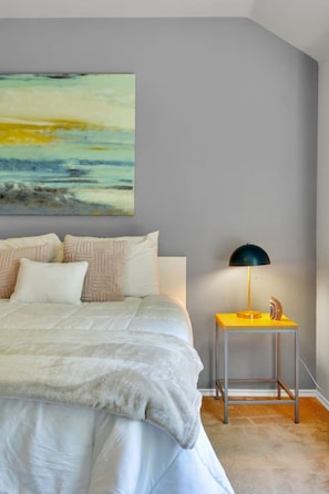 A bedroom with a bed, pillows, a bedside table with a lamp, and a large abstract painting on the wall. - Pet-Friendly Retreat | Yard, Grill + Workspace (McKinney)