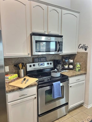 A kitchen with white cabinets, a stainless steel microwave, a stove with a pot, and a coffee sign on the wall. - Pet-Friendly Retreat | Yard, Grill + Workspace (McKinney)