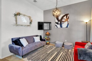A modern living room with a grey sofa, a red sofa, a black and white striped rug, a wall-mounted TV, and a contemporary art piece. - Pet-Friendly Retreat | Yard, Grill + Workspace (McKinney)
