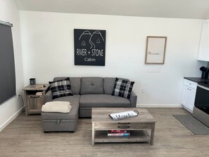 Una sala moderna con un sofá seccional gris, una mesita de centro de madera y un cuadro blanco y negro en la pared.
