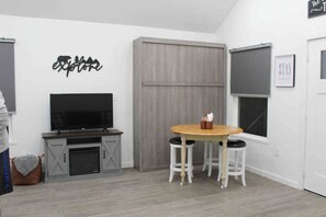 Una habitación con una televisión sobre un mueble bajo, una mesa de madera con taburetes y una puerta corrediza.