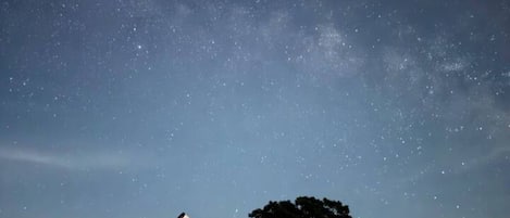 Un télescope installé sur un trépied, dans un champ, avec un arbre en arrière-plan.