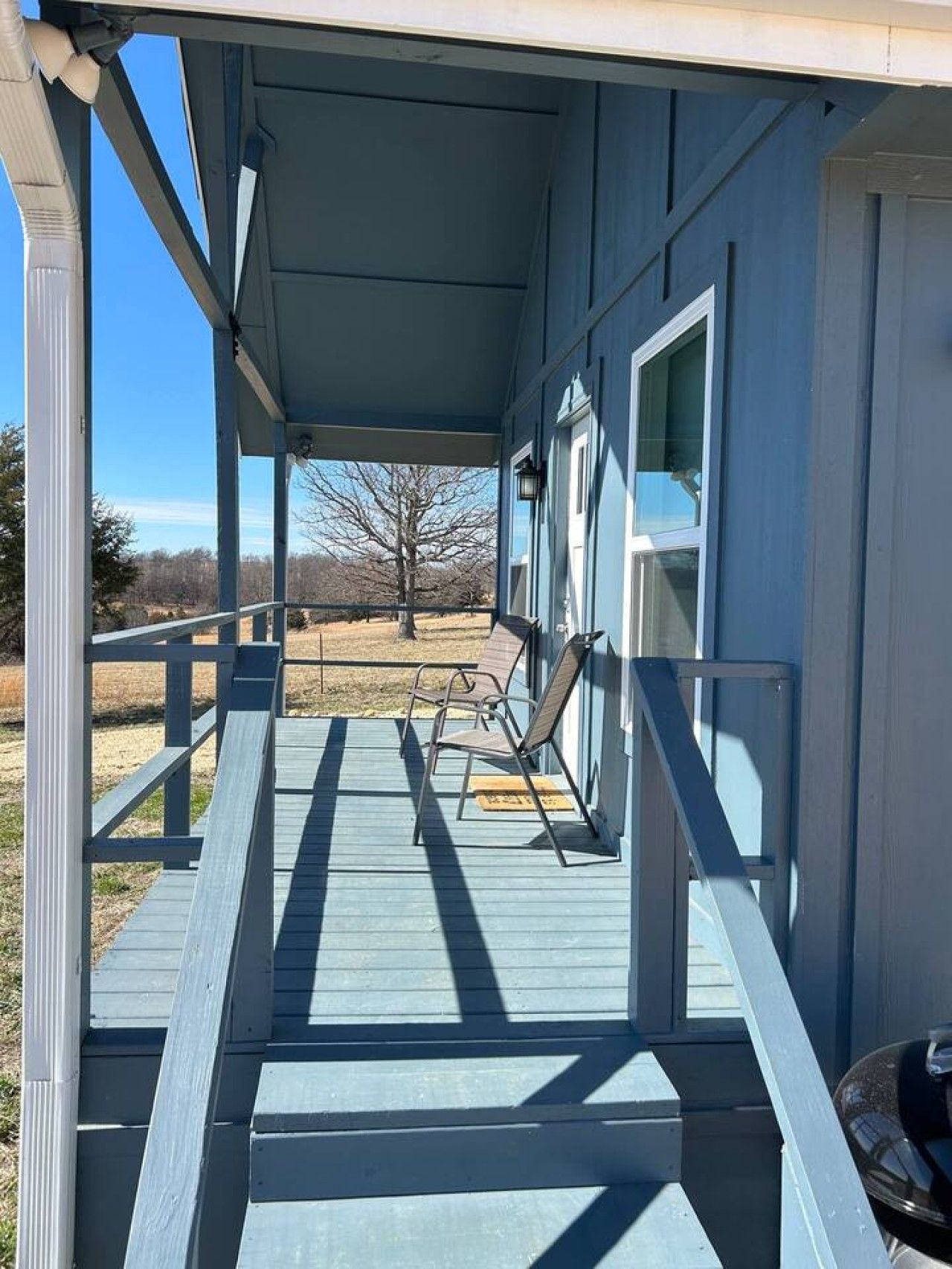 A covered porch with a wooden deck, a chair, and a door leading to a building.