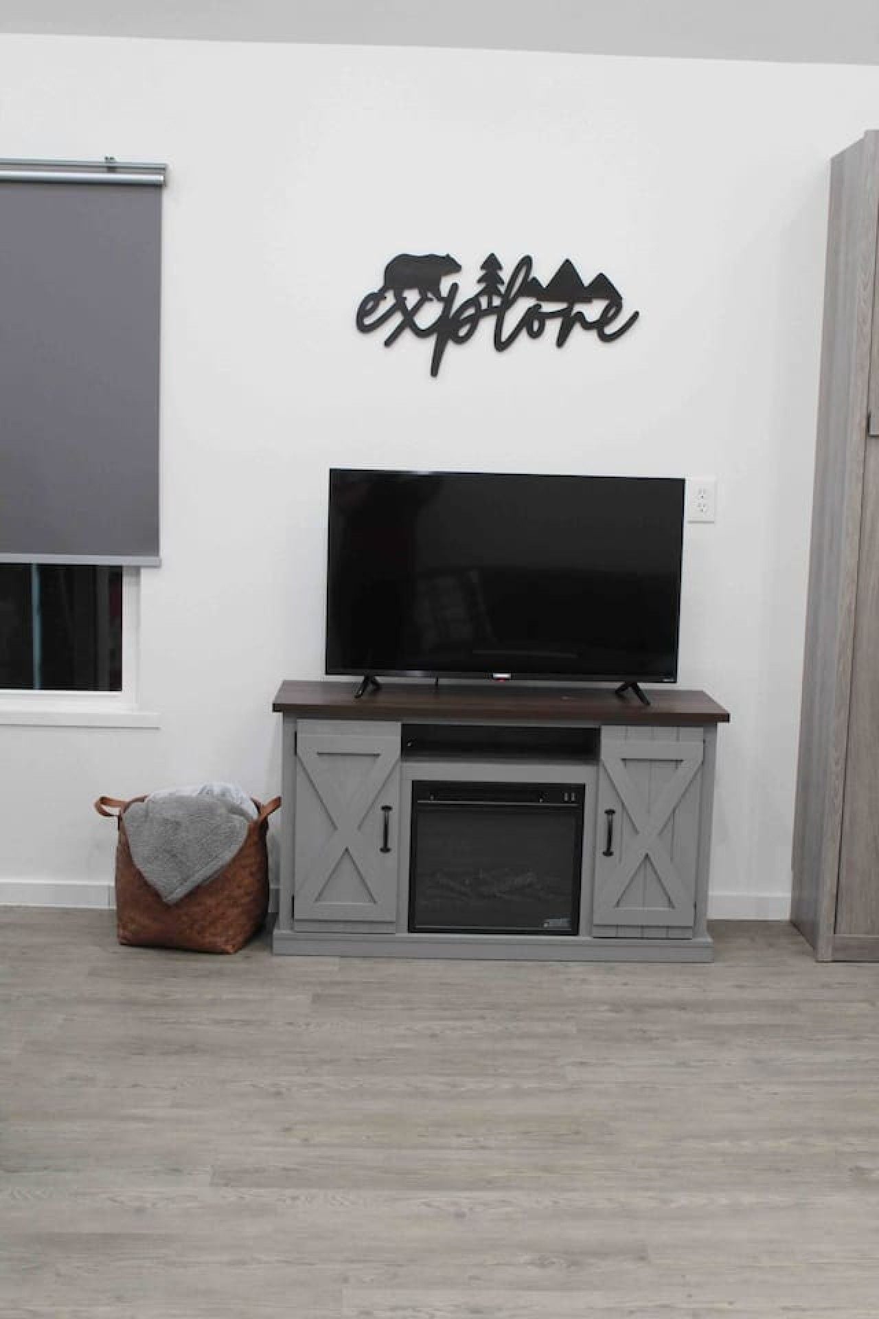Ein Zimmer mit einem Fernseher auf einem Holzständer, einem grauen Schrank darunter und einem an der Wand befestigten Schild darüber.