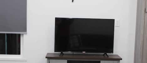 Ein Zimmer mit einem Fernseher auf einem Holzständer, einem grauen Schrank darunter und einem an der Wand befestigten Schild darüber.