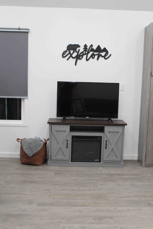 Una habitación con un televisor sobre un soporte de madera, un mueble gris en la parte inferior y un cartel en la pared.
