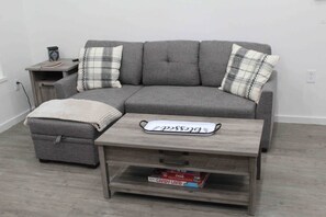 A grey sectional sofa with plaid cushions, a matching ottoman, and a wooden coffee table with a tray.