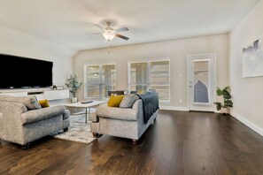 A spacious living room with a flat-screen TV, two sofas, a coffee table, and a ceiling fan. - Stylish 3BR Near Lake & Downtown w/ Patio & WiFi (Fort Worth)