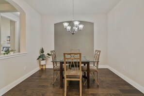 A dining room with a glass table, four wooden chairs, a chandelier, and a potted plant. - Stylish 3BR Near Lake & Downtown w/ Patio & WiFi (Fort Worth)