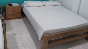 A small, single-bed room with a wooden frame, a wooden nightstand with a remote control, and a teal-colored wall.