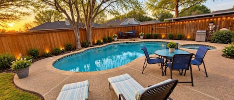 A backyard with a swimming pool, lounge chairs, and a barbecue area.