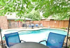 A backyard with a swimming pool, two blue chairs, and a wooden fence.