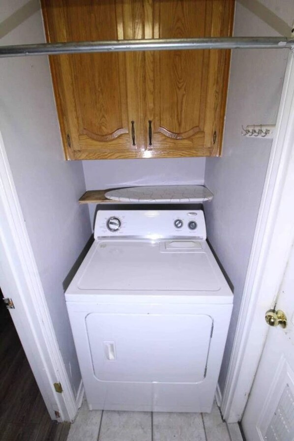 A compact laundry room with a washing machine and dryer, wooden cabinets above, and a metal rod.
