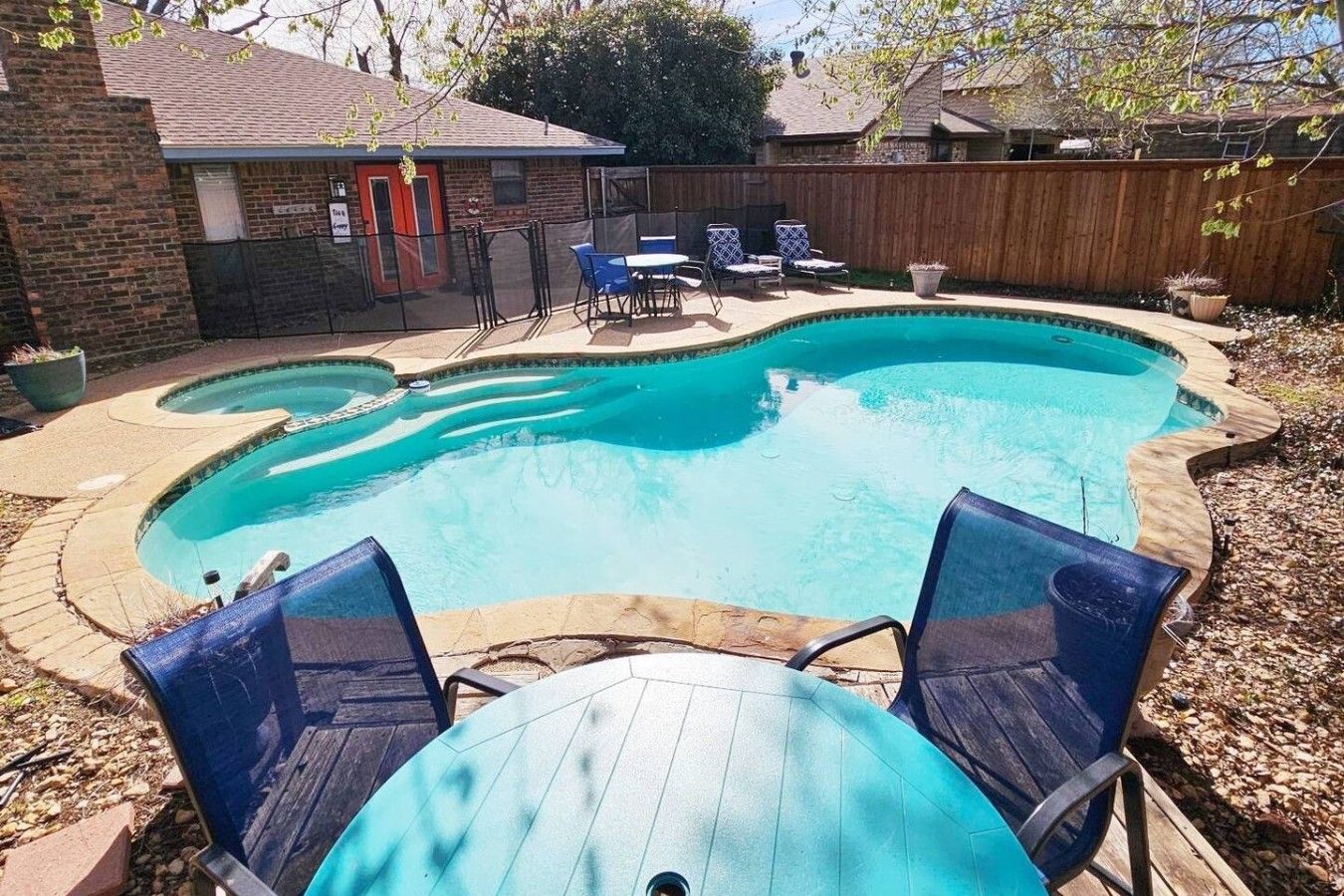 A backyard with a swimming pool, a wooden deck, and a brick house.