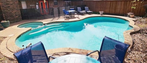 A backyard with a swimming pool, a wooden deck, and a brick house.