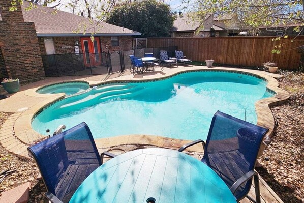 A backyard with a swimming pool, a wooden deck, and a brick house.