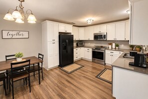 A modern kitchen with white cabinets, a black refrigerator, stainless steel appliances, and a dining area with a wooden table and chairs.