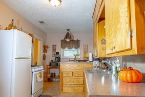 A kitchen with wooden cabinets, a white refrigerator, a stove, a microwave, and a sink. - Saint Jo 2BR Wine Country Cottage | Scenic Patio & Cozy Retreat (Saint Jo)