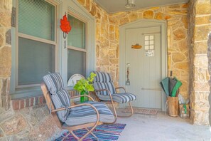 A stone exterior with a door, two striped chairs, a small table with a vase, and a welcome sign. - Saint Jo 2BR Wine Country Cottage | Scenic Patio & Cozy Retreat (Saint Jo)