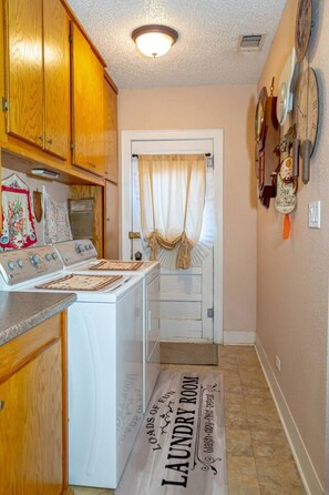 A laundry room with a washing machine, a dryer, and a rug with 'LAUNDRY ROOM' text. - Saint Jo 2BR Wine Country Cottage | Scenic Patio & Cozy Retreat (Saint Jo)