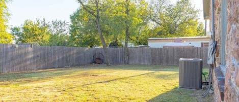 A backyard with a wooden fence, a tree, and an air conditioning unit.