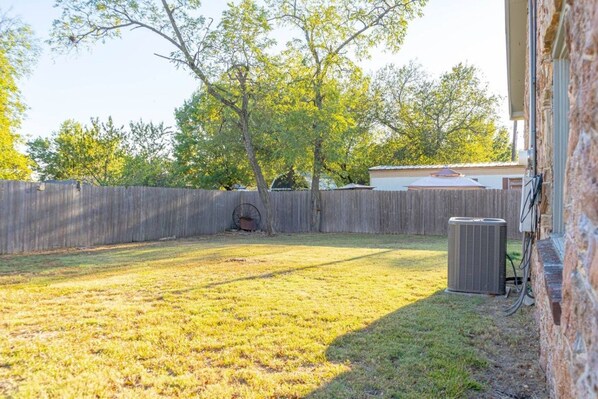 A backyard with a wooden fence, a tree, and an air conditioning unit.