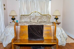 A bed with a headboard, two bedside lamps, a wooden bench, and a draped curtain.