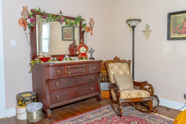 A room with a wooden dresser, a chair, a mirror with floral decorations, a floor lamp, and a rug.