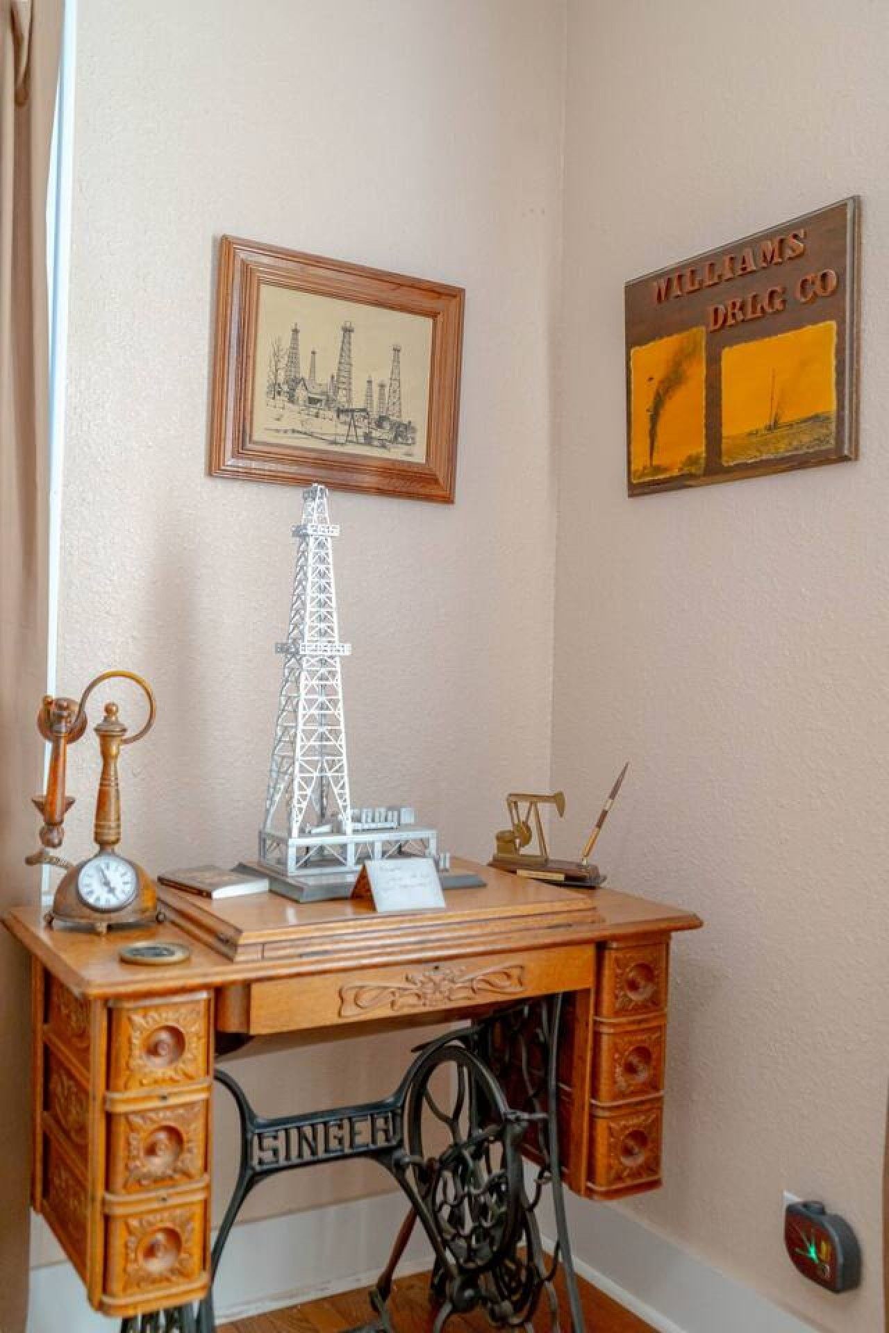 Un escritorio antiguo con una máquina de coser, una maqueta de una torre y un cuadro con la imagen de una plataforma petrolífera.