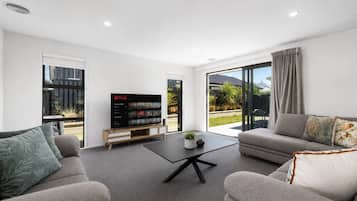 A modern living room with a flat-screen TV, two sofas, a coffee table, and a sliding glass door leading to a garden.