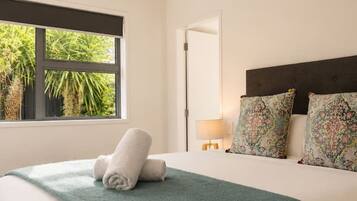 A bedroom with a bed, a window, a door, and a nightstand with a lamp.