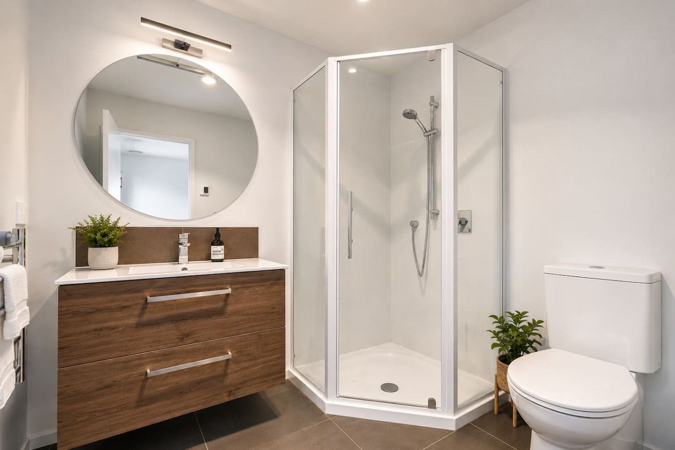 A modern bathroom with a glass-enclosed shower, a wooden vanity with a mirror, and a white toilet.