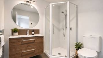 A modern bathroom with a glass-enclosed shower, a wooden vanity with a mirror, and a white toilet.