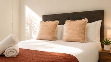 A neatly made bed with a dark headboard, two pillows, a rolled towel, and a brown knitted blanket.