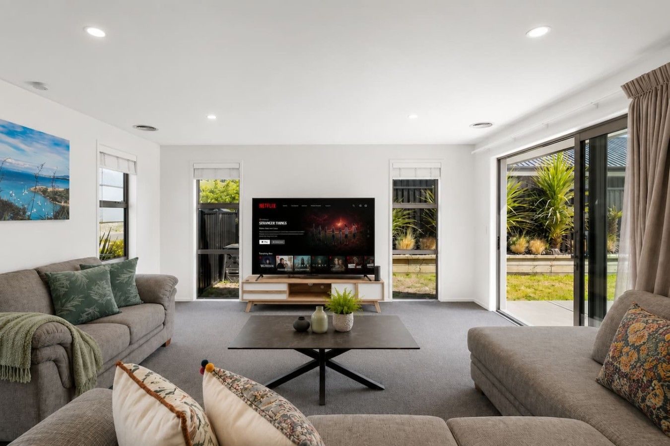 Una sala de estar moderna con un televisor de pantalla plana, dos sofás, una mesa de centro y un amplio ventanal con vistas a zonas verdes.