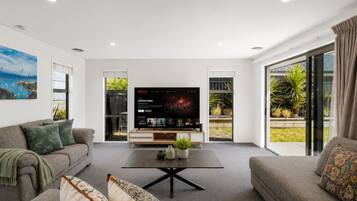 Una sala de estar moderna con un televisor de pantalla plana, dos sofás, una mesa de centro y un amplio ventanal con vistas a zonas verdes.