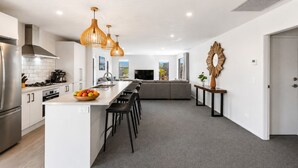 A modern kitchen with a central island, bar stools, a dining area with a sofa, and a large decorative mirror. - Mountain View - 2 Bedroom House (Queenstown)