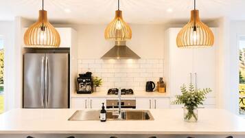 Una cucina moderna con frigorifero in acciaio inossidabile, piano cottura a gas e lavello. Tre lampade a sospensione illuminano il bancone.