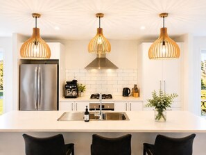 Une cuisine moderne équipée d’un réfrigérateur en acier inoxydable, d’une cuisinière à gaz et d’un évier. Trois lampes suspendues sont fixées au-dessus du plan de travail.