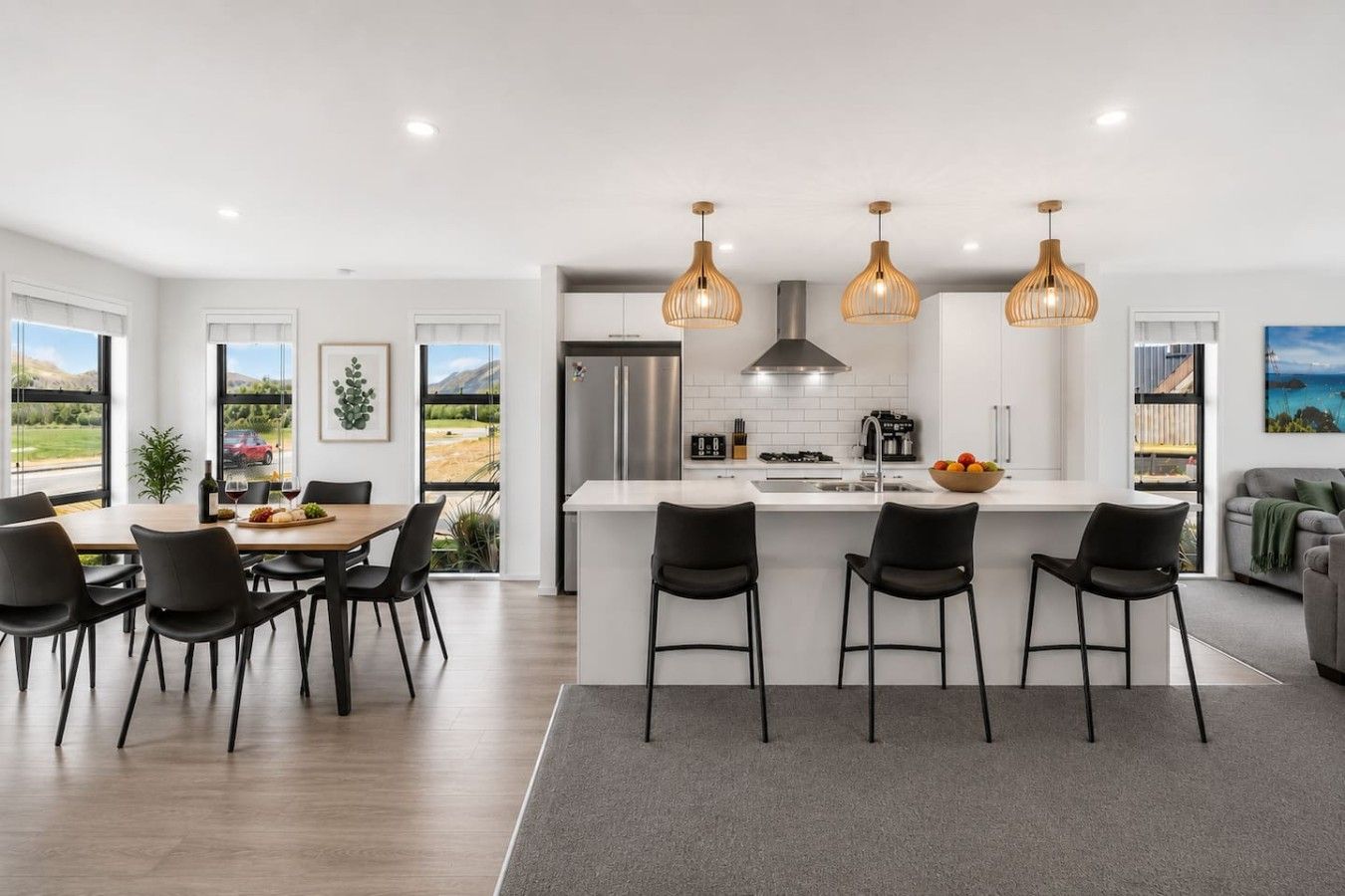 A modern kitchen with a central island, black chairs, and pendant lighting.