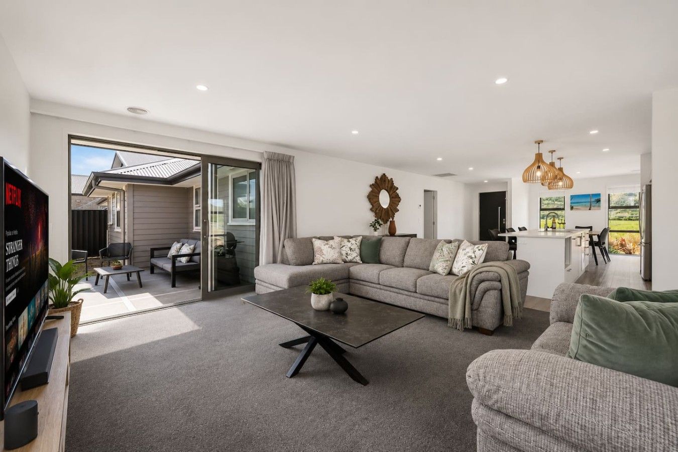 A modern living room with a sofa, coffee table, and a TV. There's a sliding glass door leading to a patio area.