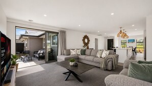 A modern living room with a sofa, coffee table, and a TV. There is a sliding glass door leading to an outdoor area. - Mountain View - 2 Bedroom House (Queenstown)