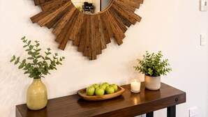 A wooden wall decor with a mirror, a wooden table with a bowl of apples, and two potted plants. - Mountain View - 2 Bedroom House (Queenstown)