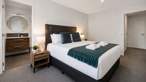 Une chambre d’hôtel moderne avec un grand lit, une table de chevet avec une lampe, un miroir et une armoire.