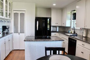 Una cocina compacta con muebles blancos, un refrigerador negro, un microondas y una cafetera.