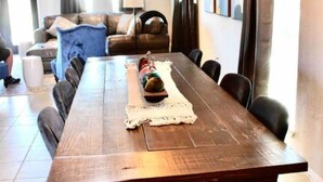Un'area pranzo con un lungo tavolo di legno, sedie, un piccolo oggetto decorativo e vista su un soggiorno con un divano e tende.